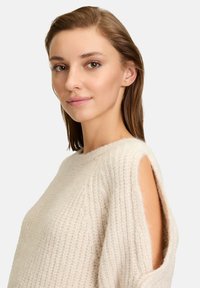 Maglione lavorato a maglia di colore crema con un motivo testurizzato, scollatura ampia e spalle scoperte per una vestibilità rilassata. Materiale morbido e confortevole.