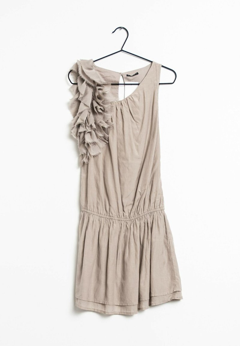 Robe beige sans manches avec un détail à volants sur une épaule, taille froncée et jupe fluide, suspendue à un cintre noir sur fond blanc.