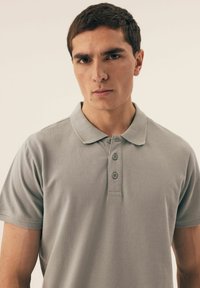 Koszulka polo w jasnoszarym kolorze z bawełny, z klasycznym kołnierzykiem i zapięciem na trzy guziki. Krótkie rękawy o gładkiej strukturze.