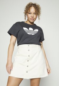 Juodas medvilninis marškinėlis su baltu Adidas logotipo, derinamas su balta džinsine A formos sijonu, kuriame yra priekiniai mygtukai ir kišenės.