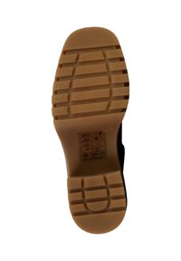 Semelle de chaussure en caoutchouc brun présentant un motif de semelle texturé, avec des rainures et un talon arrondi. Comprend des informations imprimées sur l'entretien et le matériau.