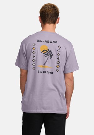 T-shirt en coton lilas avec un graphique d'un palmier et d'un soleil au dos, accompagné du texte "BILLABONG SINCE 1973" et d'accents décoratifs.