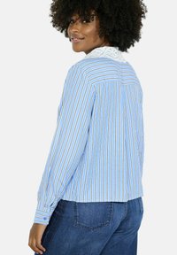 Zila svītraina garām piedurknēm blūze ar baltu acs apkakli un pogājamām aprocēm, ar maziem vertikāliem pleciem aizmugurē un brīvu piegriezumu.