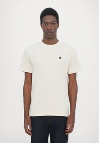 Kortermet t-skjorte med rund hals i off-white bomull, med et lite svart emblem på brystet og vanlig passform.