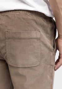Brown corduroy pants featuring a back pocket with stitching details, elastic waistband, and a textured surface.