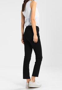 Jeans negros de corte slim, hechos de mezclilla. Presentan una cintura de altura media y un diseño clásico de cinco bolsillos. Combinados con zapatillas blancas.