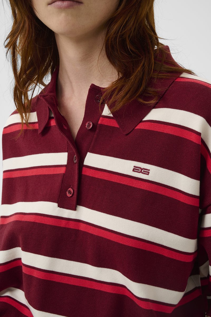 Polo rayé bordeaux et crème avec col, deux boutons au niveau du cou et un petit logo sur la poitrine. Texture douce.