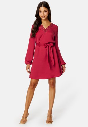 Abito rosso con maniche lunghe, scollatura in pizzo, vita con cintura e gonna svasata. Tessuto morbido con una silhouette fluida e dettagli minimi.