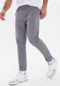 Gray cotton pants with a tapered fit, featuring rolled cuffs. Paired with white sneakers and a basic white t-shirt.
