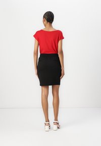 Röd kortärmad topp med bred halsringning, parat med en svart, elastisk midjeskirt i penna. Modellen bär vita blockklackade sandaler.