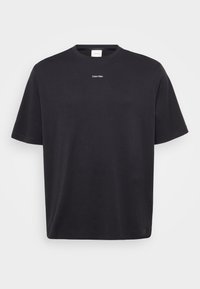 Melnas kokvilnas T-krekls ar īsām piedurknēm, apaļu kakla izgriezumu un mazu baltu "Calvin Klein" logo krūšu vidū. Gluda tekstūra.
