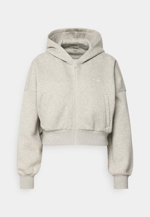 Hanorac gri cropped din material moale, prevăzut cu fermoar complet, buzunar frontal și mâneci cu manșete. Design minimalist cu glugă.