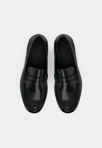 Černé kožené mokasíny s lesklým vzhledem, zdobené páskem přes přední část a viditelným prošitím kolem podrážky.