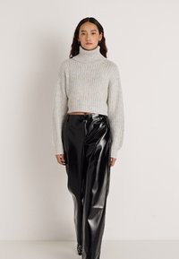 Camisola de gola alta em malha canelada cinzento claro com mangas compridas, combinada com calças largas pretas de couro sintético brilhante de cintura alta.