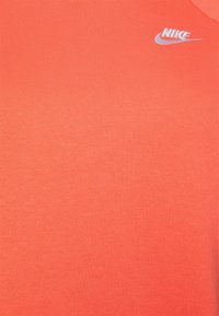 Tessuto di colore corallo con un piccolo logo Nike bianco e lo swoosh ricamati vicino all'angolo in alto a destra.