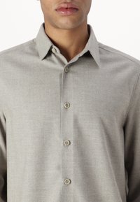Camisa abotonada de espiga gris claro con cuello puntiagudo y seis botones. La tela tiene una textura suave y un patrón sutil.