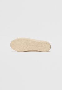 Beige skinnesåle med en teksturert overflate som har bølgete mønstre og en ribbet kant. Materialet ser gummiaktig ut med en matt finish.