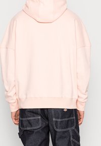 Różowa bluza z kapturem o luźnym kroju, z opuszczonymi ramionami i ściągaczami na rękawach, zestawiona z ciemnymi spodniami cargo z denimu.