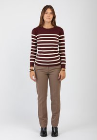 Camicetta a righe maroon e crema con maniche lunghe e orlo a coste, abbinata a pantaloni attillati beige e stivaletti neri alla caviglia.