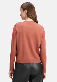 Różowy sweter dzianinowy z długimi rękawami, prążkowanym dołem i mankietami. Noszony na czarnych skórzanych spodniach, z prostym okrągłym dekoltem.