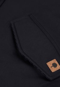 Tessuto blu navy con una superficie liscia presenta una tasca con un accento in sughero e cuciture a contrasto. Il design è semplice e funzionale.