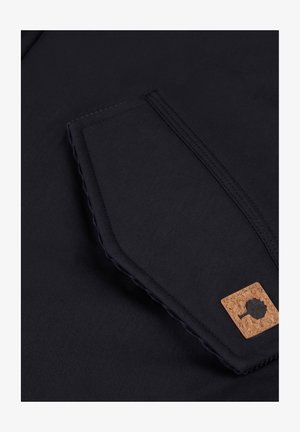 Tessuto blu navy con una superficie liscia presenta una tasca con un accento in sughero e cuciture a contrasto. Il design è semplice e funzionale.
