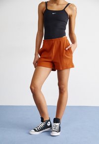 Svart ärmlös bodysuit med en liten vit logotyp, parat med orange ribbade shorts med fickor. Svarta högstövel sneakers fulländar looken.