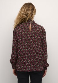 Blouse à manches longues en tissu marron, ornée d'un motif floral en rose et crème. Détail en forme de clé à l'arrière du cou, coupe décontractée.