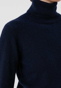 Suéter de cuello alto en azul marino, confeccionado con un tejido suave y texturizado; presenta un diseño ajustado y un cuello acanalado. Sin patrones ni acentos visibles.