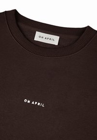 Hnedý sveter s rebrovaným golierom, s malým bielym logom "OH APRIL" na hrudi. Mäkký materiál, jednoduchý a čistý dizajn.