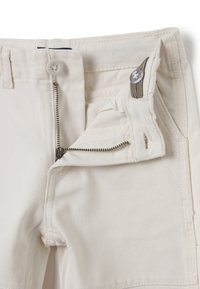 Pantalones blancos con cierre de cremallera y botón. Incluyen características como una textura suave, costuras reforzadas y una pequeña etiqueta de marca en la cintura.