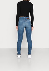 Blå skinny jeans i denim, med bakfickor, medelhög midja och en brun läderlapp vid midjan.