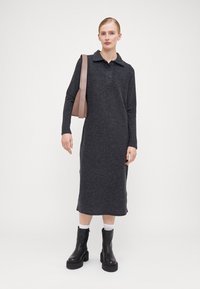 Rochie tricotată de culoare gri închis, cu mâneci lungi, guler și nasturi. Asortată cu cizme groase negre și o geantă de umăr bej. Textură netedă.