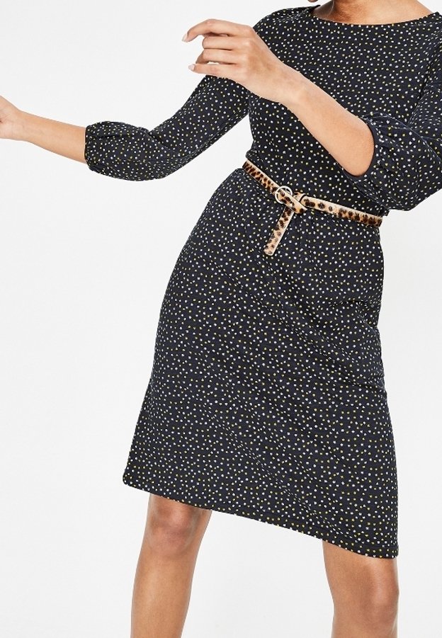 Femme portant une robe noire à petits pois blancs et jaunes, manches trois-quarts, et une ceinture imprimé léopard à la taille.
