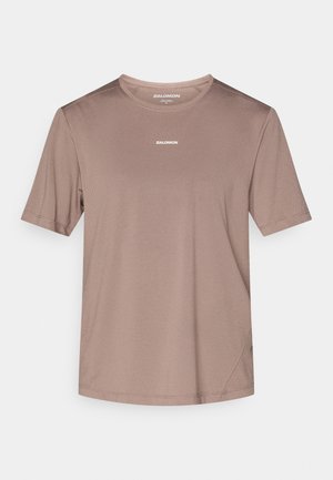 Világosbarna rövid ujjú atlétikai póló, texturált anyagból készült, kerek nyakkivágással és egy kis fehér logóval a mellkason.