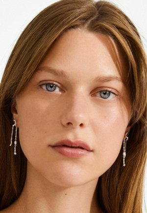 Pendientes colgantes de plata con cadenas y detalles de cuentas redondas. El estilo combina minimalismo y detalles intrincados para un look moderno.