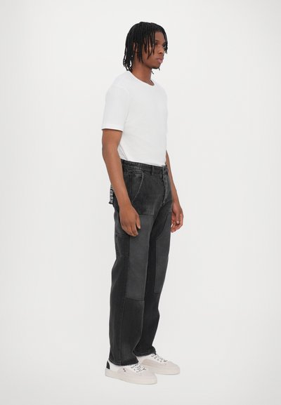 Pantalons en denim noir avec des patchs contrastants, coupe décontractée et taille élastique, associés à une simple chemise blanche à manches courtes et des baskets.