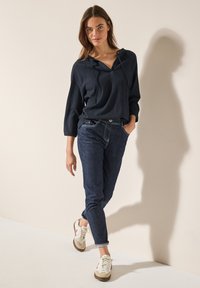 Marinblå ribbad hoodie med v-ringning och dragsko, som matchas med mörka jeans och ljusa sneakers med röda accenter och beige sulor.