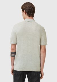 Lys grå kortærmet polo skjorte med tekstureret stof, klassisk krave og diskrete detaljer bagpå, parret med mørke jeans.