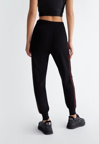Schwarze Jogginghose aus weichem Stoff, mit roten Seitenstreifen, gerippten Bündchen und einem bequemen elastischen Bund.