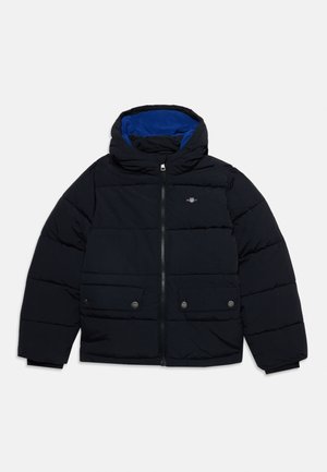 Giacca imbottita nera con fodera blu, cappuccio, cerniera frontale, due tasche con bottoni a pressione e piccolo logo sul petto su sfondo uniforme.
