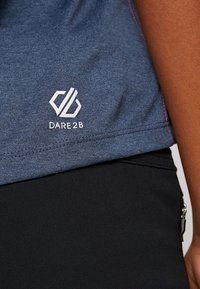 Niebieska sportowa koszulka z krótkim rękawem o teksturowanej tkaninie, z białym logo "DARE2B" blisko dolnego brzegu i kontrastowymi różowymi przeszyciami.