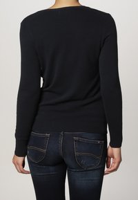 Black long-sleeve sweater made of soft knit material, fitted design, with a rounded neckline and seamless shoulders. Paired with blue jeans.