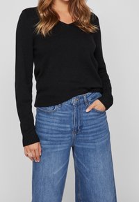 Pull noir à col en V avec manches longues, associé à un jean en denim bleu clair taille haute, à la coupe décontractée et à la légère décoloration.