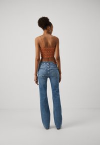 Top corto e a fantasia arancione con spalline sottili, abbinato a jeans a vita alta di colore blu a zampa, mostrando una superficie in denim liscia.