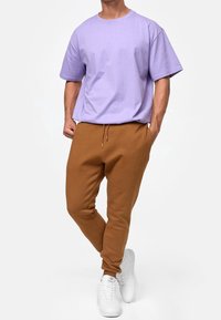 Lavendel bomulds T-shirt med korte ærmer, parret med brune joggingbukser med elastisk talje og sidelommer, kompletteret med hvide sneakers.