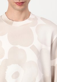 Helle beigefarbene Sweatshirts mit großen, abstrakten Blumenmustern in einem etwas dunkleren Farbton. Mit Rundhalsausschnitt, weichem Stoff und eingeprägtem Logodesign.