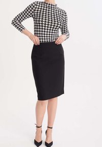 Dlouhý rukáv s černobílým kostkovaným vzorem, zkombinovaný s úzkou černou tužkovou sukní. Má elegantní design a hladkou texturu.