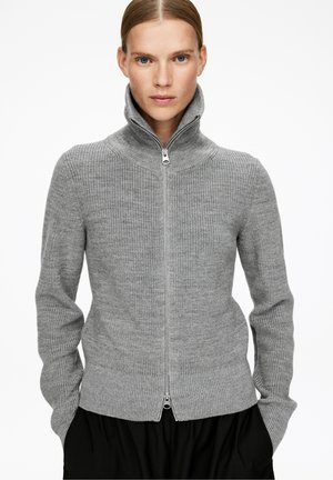 Grauer Reißverschluss-Pullover mit hohem Kragen, geripptem Muster und langen Ärmeln. Verfügt über einen silbernen Reißverschluss und einen taillierten Saum. Einfaches, klares Design.