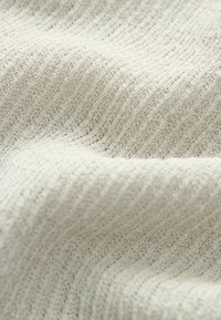 Licht beige stof met een gestructureerd, geribbeld ontwerp, dat fijne gebreide patronen toont. Zachte, lichte en licht rekbare stof.